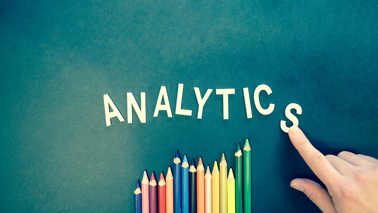 Home Colored pencils and letters spelling 'ANALYTICS' on a textured background with a hand.